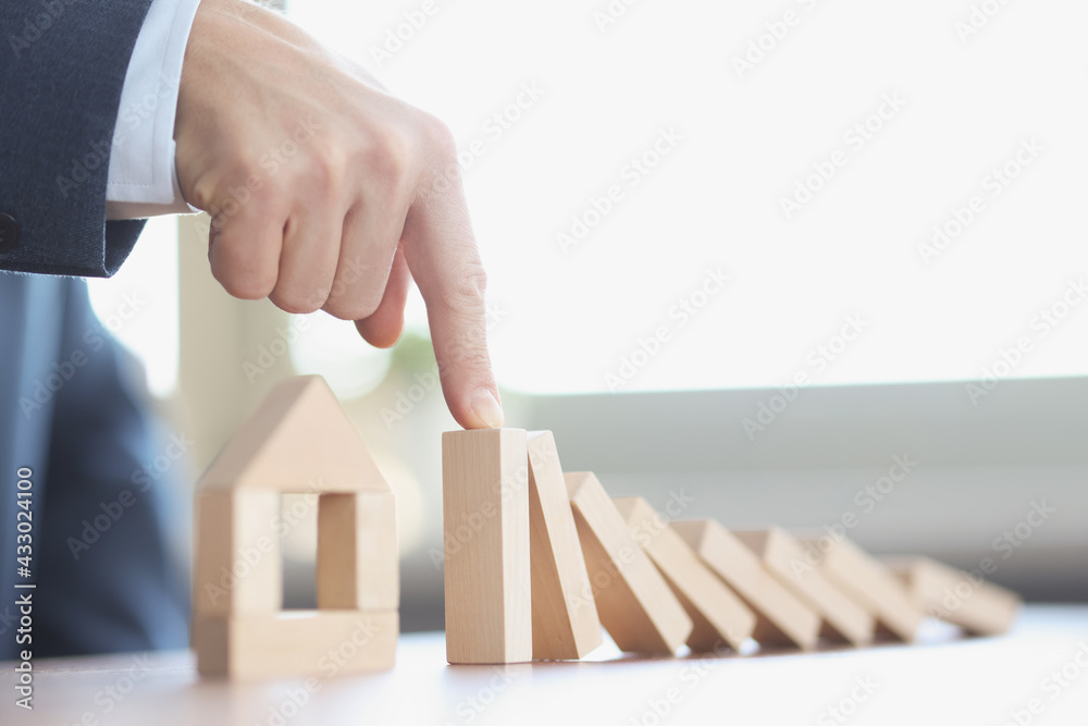 Male hand stopping falling wooden blocks in front of toy house closeup Male hand stopping falling wooden blocks in front of toy house closeup