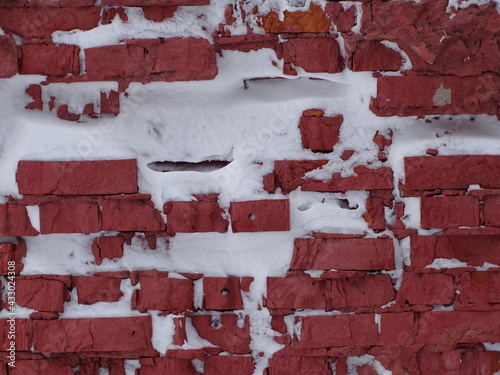 Old red brick wall with adhered white snow 