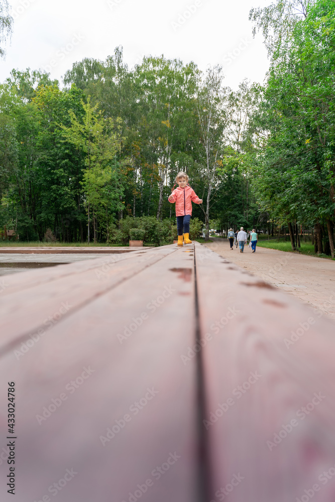 Fototapeta premium little girl walking on a wooden path in the park after the rain, copy space. Shallow depth of field