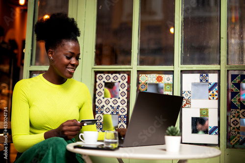 African woman in cafe makes a purchase on the Internet. Beautiful woman on the laptop with credit card.