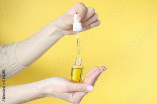 Female hands holding bottle of cosmetic oil on yellow background closeup