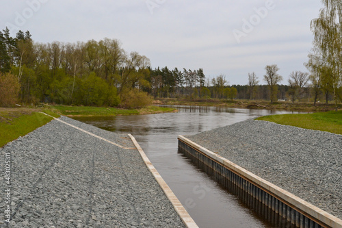 View of the source of the canal lock in the river, which is surrounded on both sides by a shore covered with white stones.