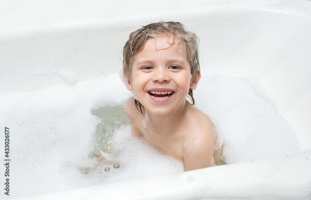 the child sits in the bath in the water with foam and laughs, makes a funny expression on his face. concept baby loves to wash the child sits in the bath in the water with foam and laughs, makes a funny expression on his face. concept baby loves to wash
