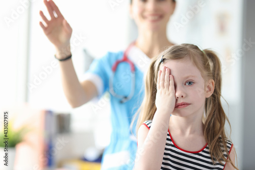 Little girl covering her eyes with her hand at ophthalmologist appointment