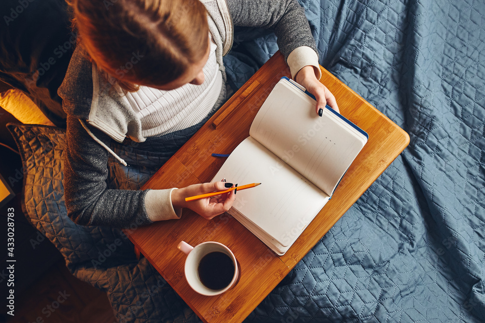 Obraz premium Student learning at home. Young woman making notes, reading and learning from notepad. Girl writing journal sitting in bed