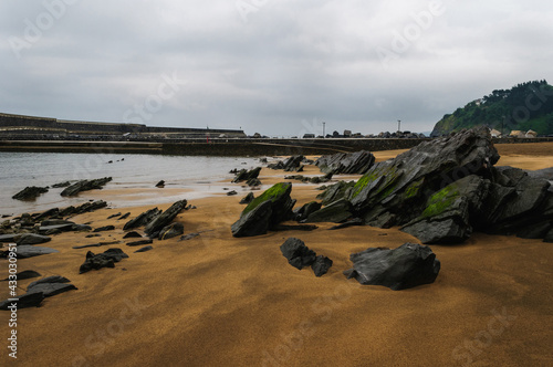 Golden sand beach and stones with seaweed with harbor background and cloudy sky photo