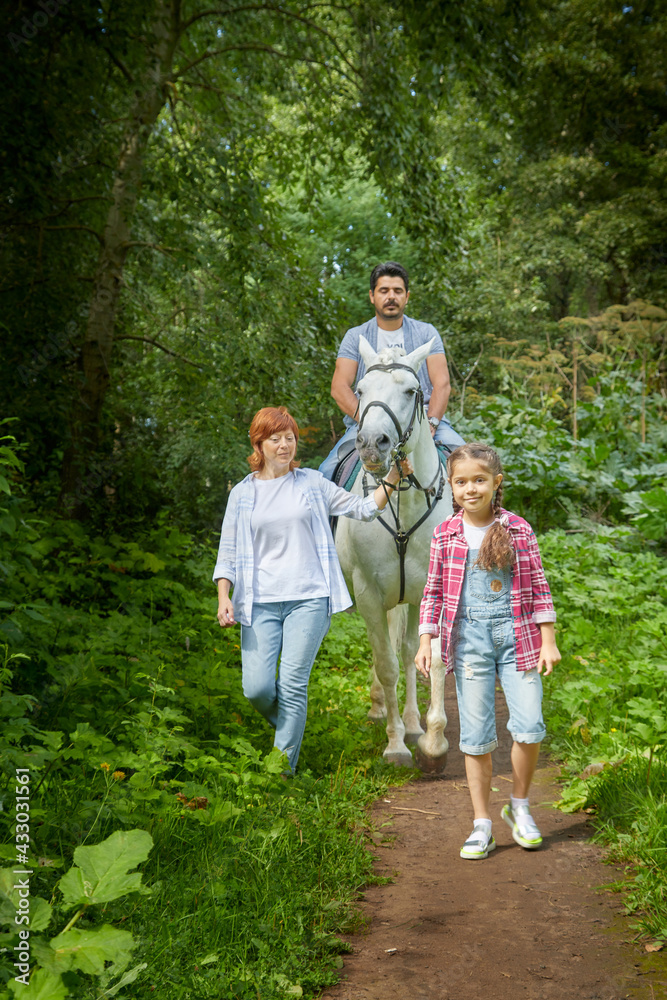 Kirov, Russia - August 07, 2020: A family including a mother, father and daughter walks and rides a horse in nature among green trees. Man, woman, girl with horse in nature in summer Kirov, Russia - August 07, 2020: A family including a mother, father and daughter walks and rides a horse in nature among green trees. Man, woman, girl with horse in nature in summer