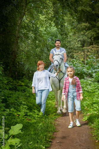 Kirov, Russia - August 07, 2020: A family including a mother, father and daughter walks and rides a horse in nature among green trees. Man, woman, girl with horse in nature in summer