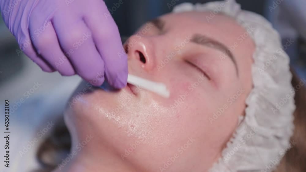 Woman beautician applies liquid to woman's face with cotton swabs. Woman beautician applies liquid to woman's face with cotton swabs.