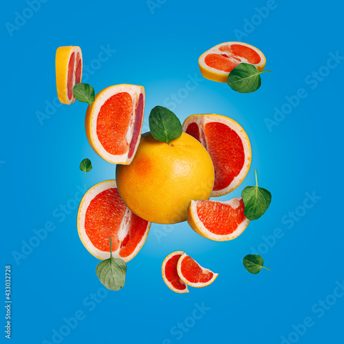 Grapefruit with flying slices and leaves on vibrant blue background. Creative summer fruit food concept. Trendy vegetarian vitamin diet or juice tropical bar idea.