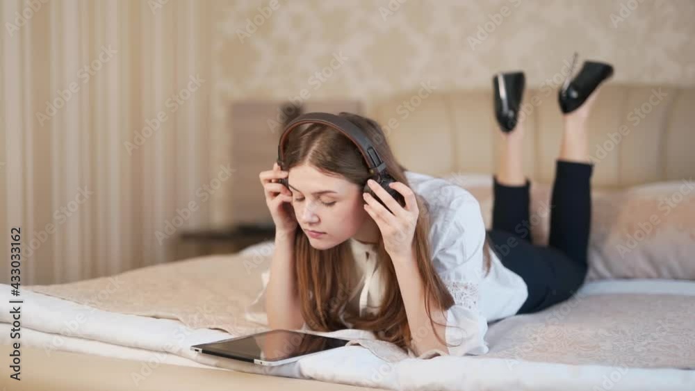 Beautiful woman lying on the bed in headphones and with a tablet Beautiful woman lying on the bed in headphones and with a tablet