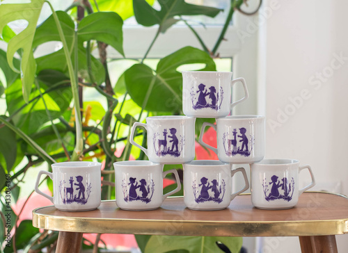 Vintage porcelain cup collection with shadow scene pattern on a wooden table with plants in the background