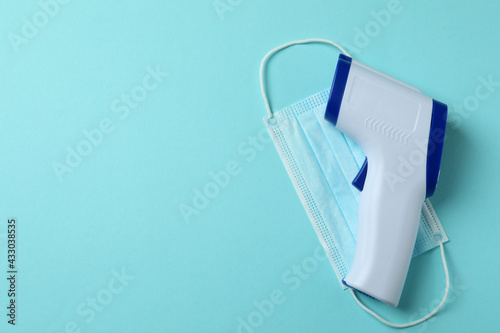 Thermometer gun and medical mask on blue background
