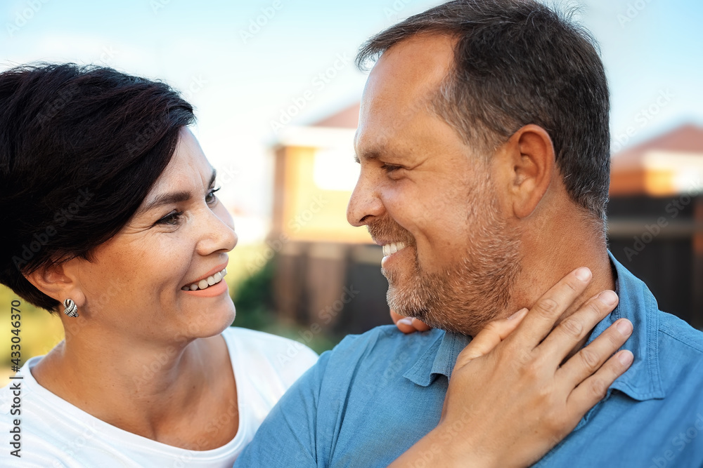 Fototapeta premium Portrait of a happy married couple in close-up. Wife gently hugs middle-aged husband outdoors and smiles