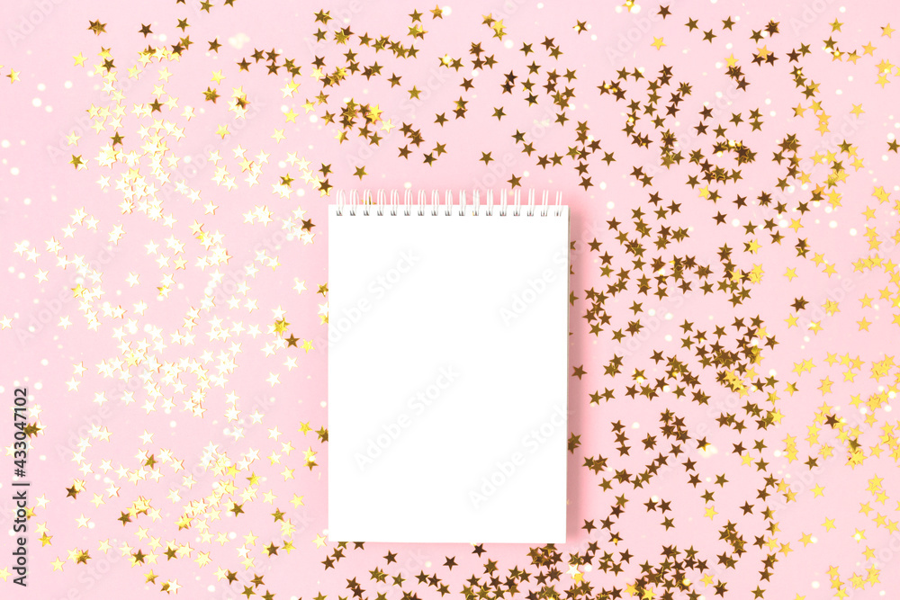 Notebook mockup on a pink background with gold stars confetti. Festive flatlay with copy space.