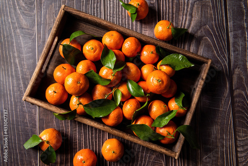 Fresh ripe tangerines with green leaves on black wooden table, closeup
