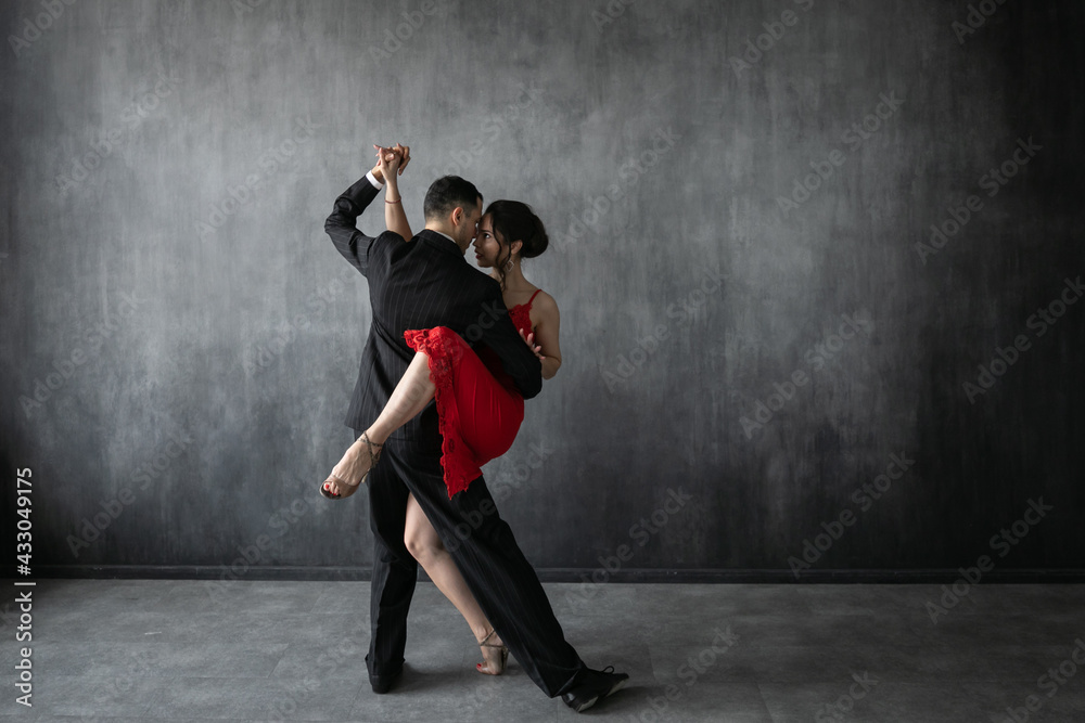 Couple of professional tango dancers in elegant suit and dress pose in a dancing movement on dark background. Attractive man and woman dance looking eye to eye. - obrazy, fototapety, plakaty 