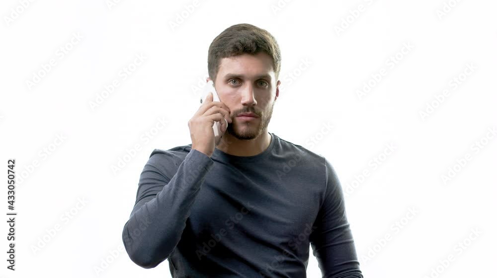 Slow motion close up of serious confident handsome smart young adult man holding a mobile phone over white background. Brunette bearded millennial professional looking at camera.
