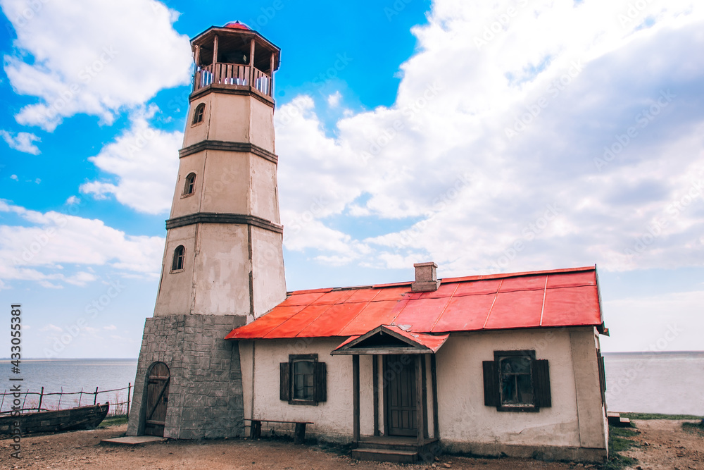 An old lighthouse and a house with a red roof on the beach
