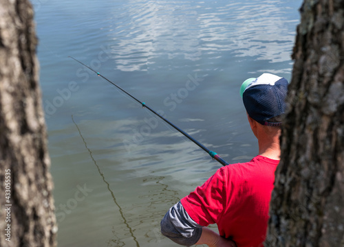 A man stands with a fishing rod on a lake and catches fish on a sunny summer day.