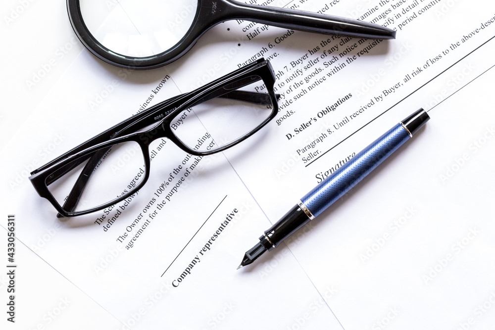 Fototapeta premium Pen and glasses lying on signed documents on office desk top view