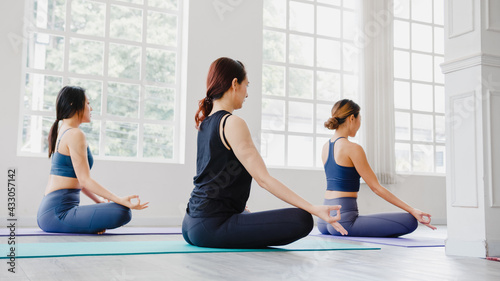 Young Asian sporty attractive people practicing yoga lesson with instructor. Asia group of women exercising healthy lifestyle in fitness studio. Sport activity  gymnastics or ballet dancing class.