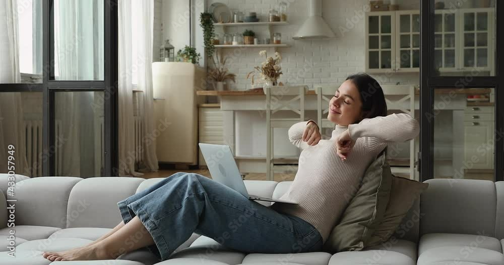 Young freelancer woman sit on comfy sofa at home finish work on laptop resting take break stretching back with raised arms, making exercised for muscles, feeling satisfied ending telecommuting concept