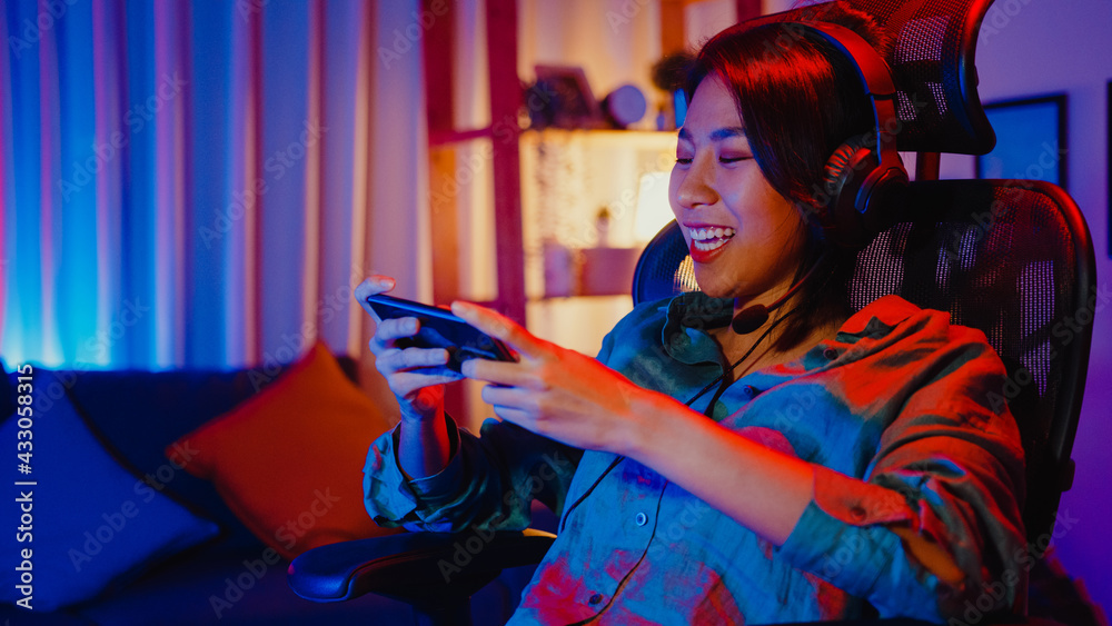 Happy Asia Girl Gamer Wear Headphone Competition Play Video Game Online  With Smartphone Colorful Neon Lights In Living Room At Home. Esport  Streaming Game Online, Home Quarantine Activity Concept. Stock Photo,  Picture