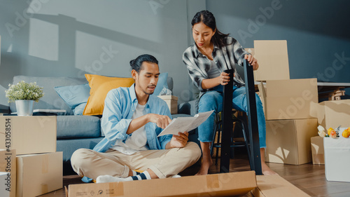 Fotografie Happy asian young attractive couple man and woman help each other unpacking box and assemble furniture decorate house build table with carton box in living room