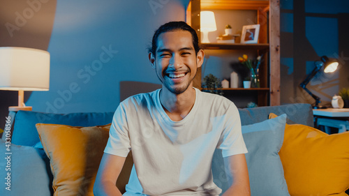 Happy young freelance asian man looking at camera smile and talk with friends on video call online at night in living room at home, Stay at home quarantine, work from home, Social distancing concept.