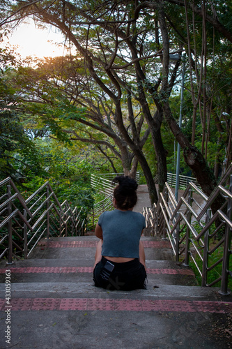curly latin girl relax on tropical road, curly latin woman sitting in a tropical park