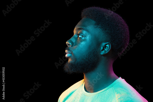 African young man's portrait on dark studio background in neon. Concept of human emotions, facial expression, youth, sales, ad.