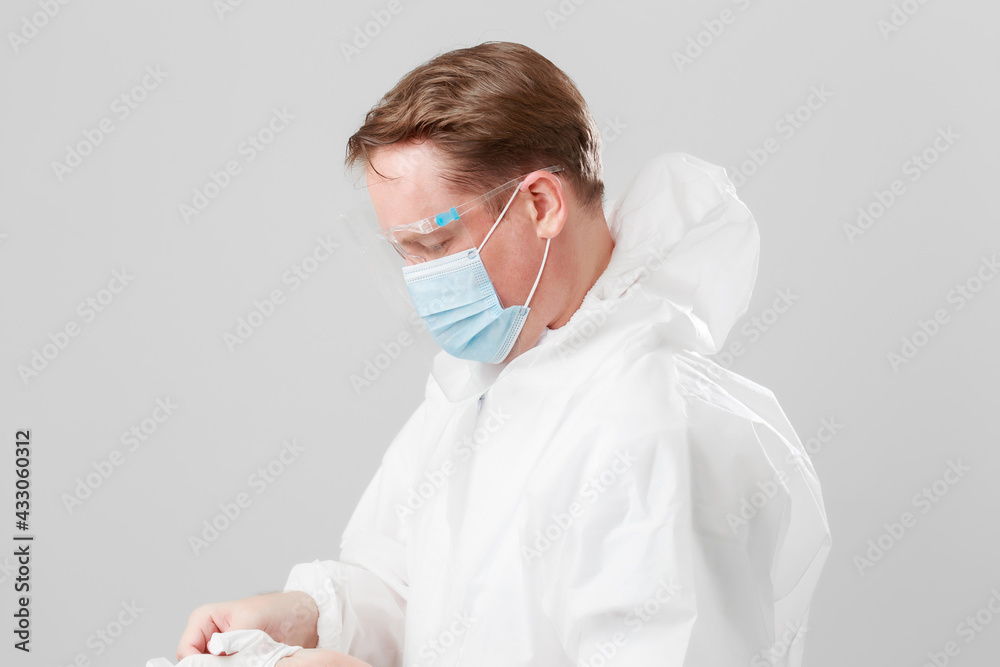 Young Caucasian men in hazmat suit wearing surgical face mask and face shield during Coronavirus pandemic prevention. Young physician doctor in protective ppe suit wearing latex gloves.
