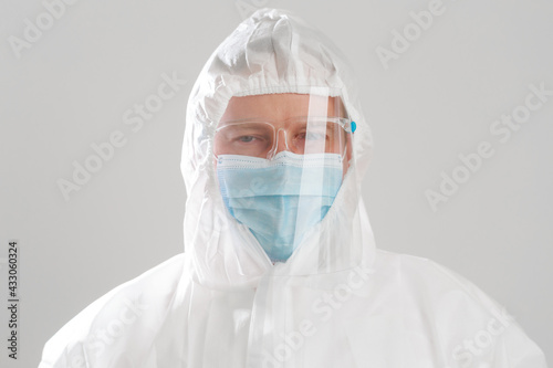 Young Caucasian men in hazmat suit wearing surgical face mask and face shield during Coronavirus pandemic prevention. Close up doctor in protective PPE suit looking at camera.