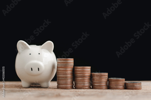 Saving money and business financial concept, white piggy bank and coin stacked of money look like graph to show step to keep money, plan for the future on black background.