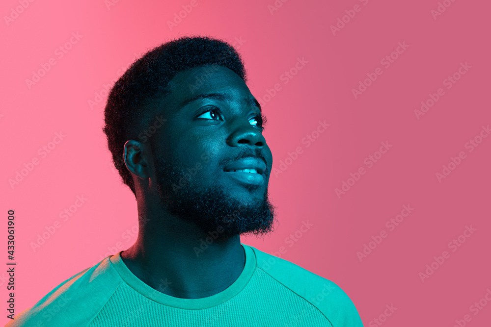 Obraz premium African young man's portrait on pink studio background in neon. Concept of human emotions, facial expression, youth, sales, ad.