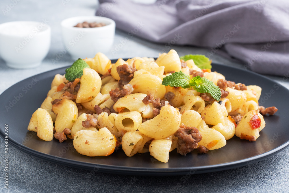 Stewed pasta with minced beef and vegetables, macaroni in Navy style on a plate. grey concrete background. Stewed pasta with minced beef and vegetables, macaroni in Navy style on a plate. grey concrete background.