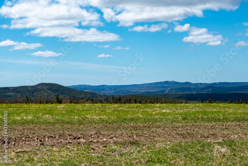 A bright blue sky meets rural barren tundra, parched earth. The peat moss is yellow and there's very little green grass on the land. The dry bare countryside has a steady incline to the rocky hill.