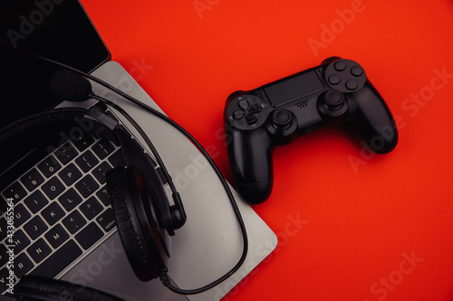 Laptop with headphones, black gamepad on red background. Gaming and cybersport concept