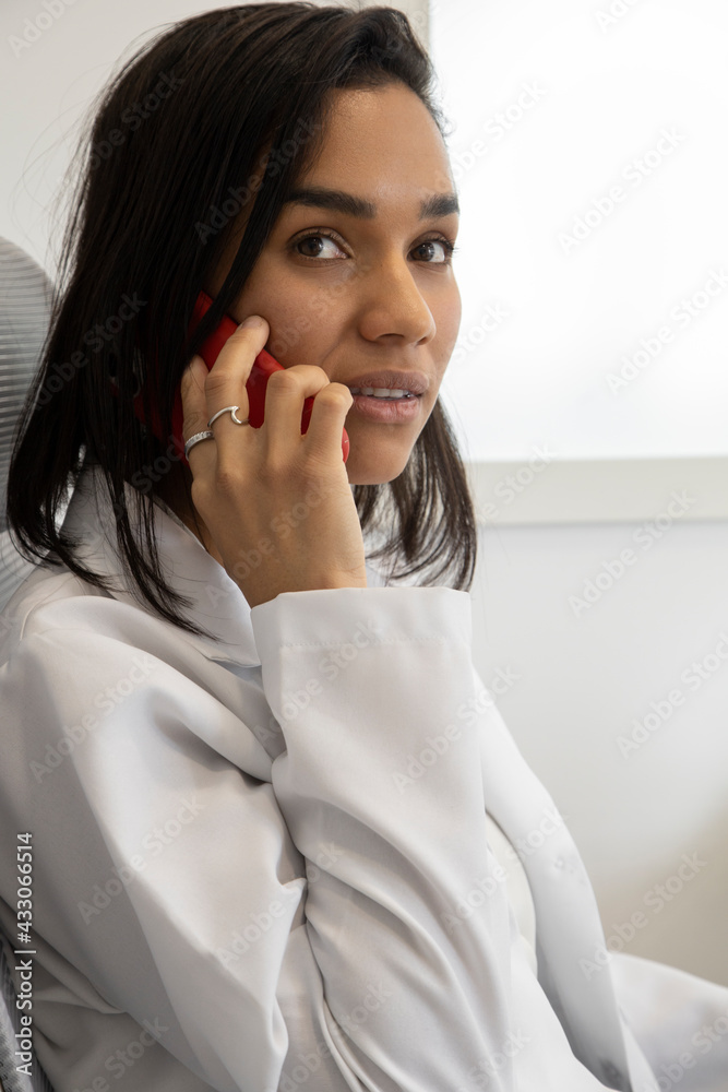 doctor's office, there is a beautiful young latin health professional with short hair sitting at the desk talking on cell phone, medicine doctor's office, there is a beautiful young latin health professional with short hair sitting at the desk talking on cell phone, medicine