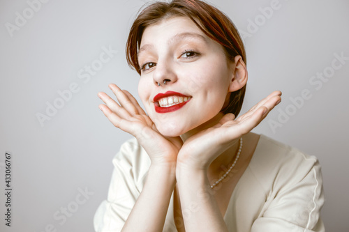 A happy woman with red lips and white teeth, smiling, holding her hands near her face