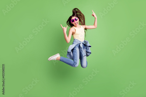 Full length photo of young girl happy positive smile jump show fingers rock sign isolated over green color background