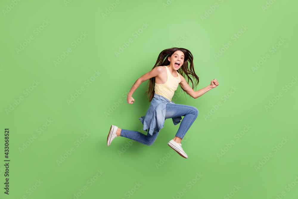 Full body profile side photo of young girl happy positive smile jump go walk run hurry isolated over green color background Full body profile side photo of young girl happy positive smile jump go walk run hurry isolated over green color background