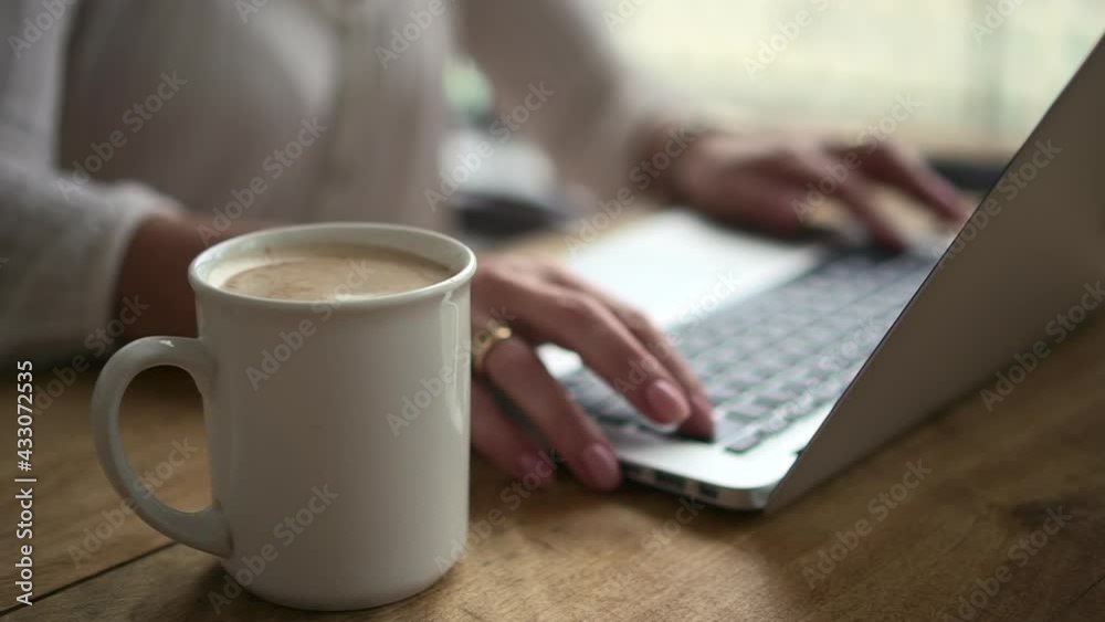 Closeup view of woman working with laptop and sitting at table with coffee in home office. Closeup view of woman working with laptop and sitting at table with coffee in home office.