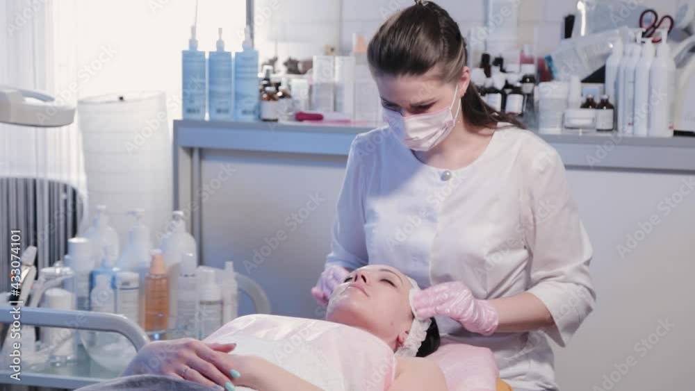 Woman beautician wipes woman face with cotton pad. Woman beautician wipes woman face with cotton pad.