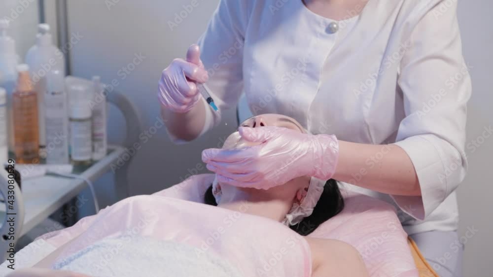 Woman beautician applies peeling from a syringe to her face.