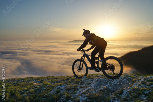 Mountain Biker Riding Downhill  Above the Clouds at Sunset. © StockVisual