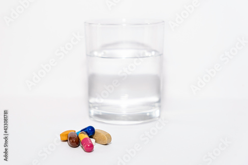 close up of colorful pill capsule vitamins supplement with glass of water on white background close up
