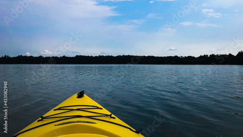 Front of a kayak on the water. Trees and the shore can be seen.