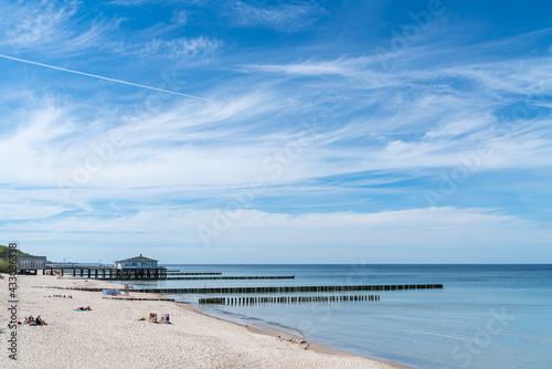 A view of the beach and a wooden building at the end of a wooden pier  with a row of  breakwaters in the foreground.